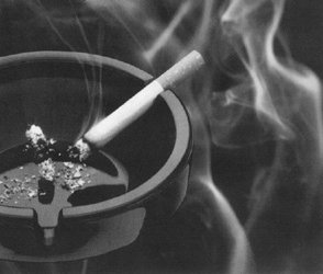 Cigarette sits smoking in black ashtray in black and white photo.