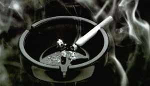 Cigarette sits smoking in ashtray's cigarette holder.