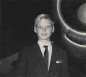 Patrick stands in a suit and tie in front of a Delta 707 plane engine in black and white photograph.